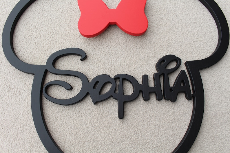 May include: Black wooden cutout of Mickey Mouse ears with a red bow on top and the name "Sophia" written in a stylized font.