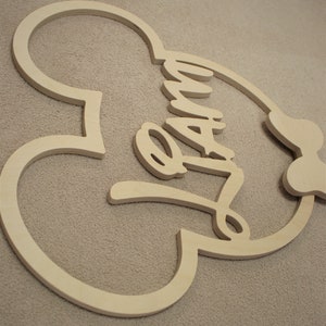 May include: Wooden cutout of a Mickey Mouse head with the word "Family" written inside. The cutout is unfinished and ready to be painted.