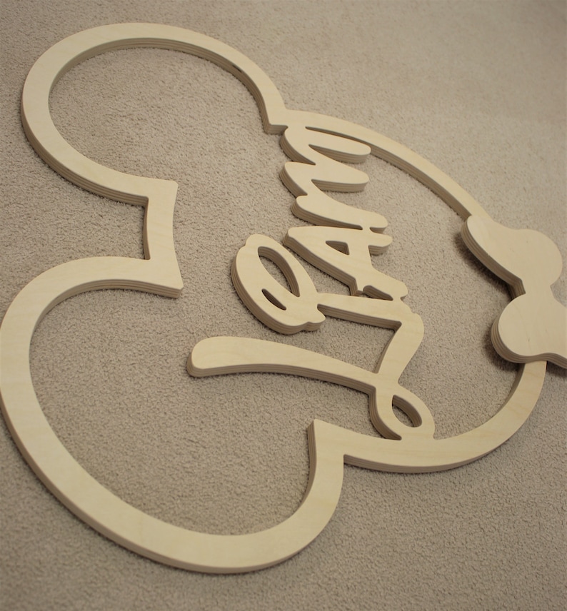 May include: Wooden cutout of a Mickey Mouse head with the word "Family" written inside. The cutout is unfinished and ready to be painted.