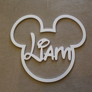 May include: White wooden cutout of Mickey Mouse's head with the name "Liam" written in a stylized font inside.