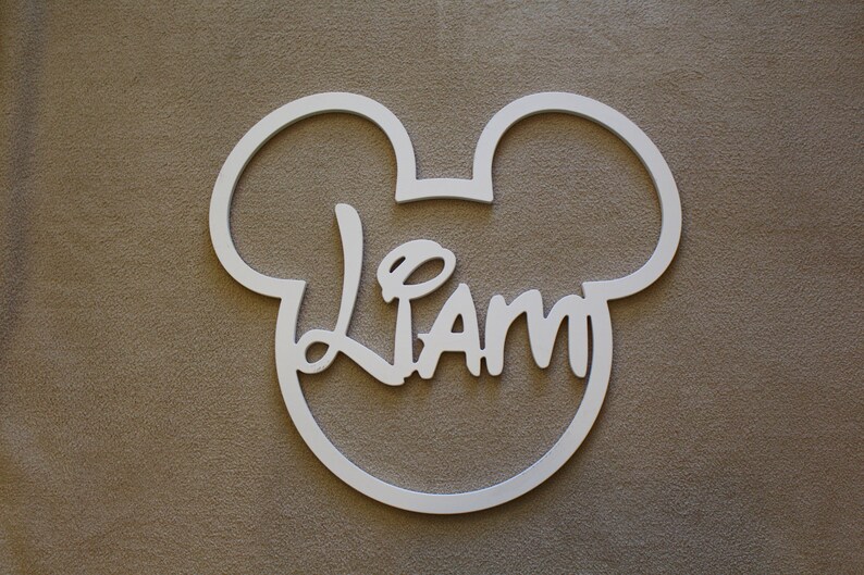 May include: White wooden cutout of Mickey Mouse's head with the name "Liam" written in a stylized font inside.
