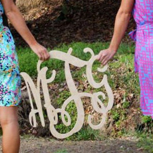 May include: Two people holding a large wooden monogram sign with the letters "MEG" in a cursive script.