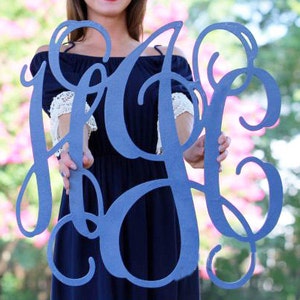 May include: A large, blue, wooden monogram sign with the letters "HOC" in a decorative script font. The sign is being held by a person.