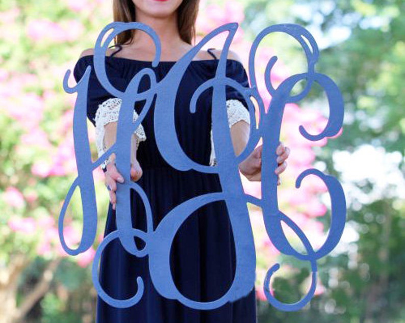 May include: A large, blue, wooden monogram sign with the letters "HOC" in a decorative script font. The sign is being held by a person.