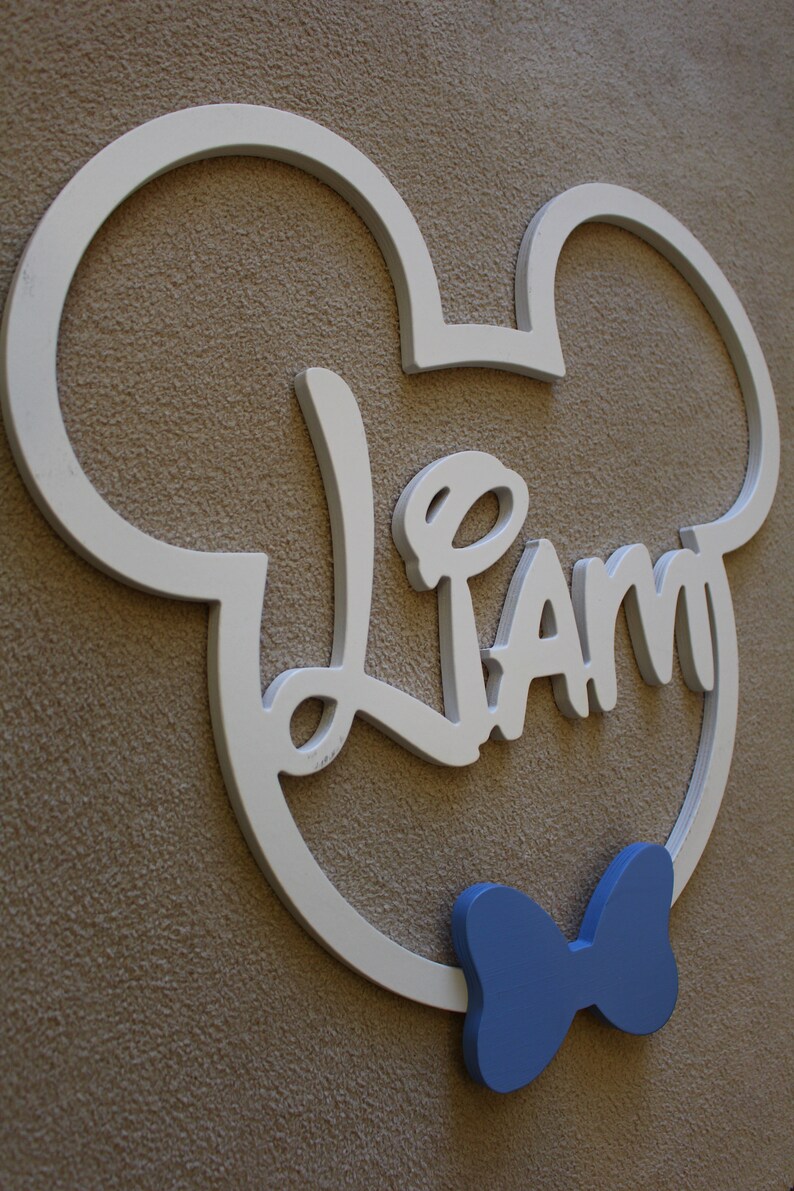 May include: White wooden Mickey Mouse head cutout with the name "Liam" in cursive lettering and a blue bow tie.