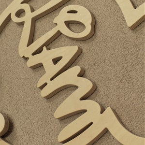 May include: Wooden sign with the word "Family" written in a cursive font. The sign is made of multiple layers of wood, giving it a 3D effect.