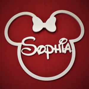 May include: White wooden cutout of Mickey Mouse ears with a bow in the center and the name "Sophia" written in a stylized font.