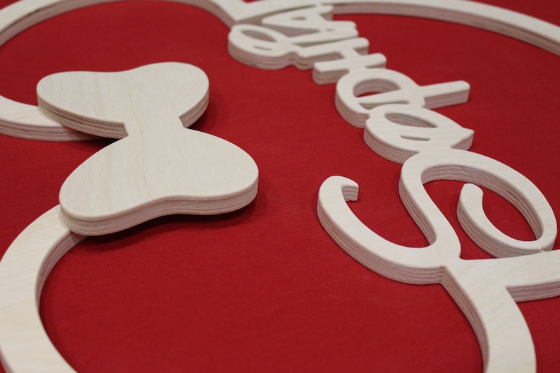 May include: A wooden cutout of Mickey Mouse ears with a bow on the left side. The ears are shaped like a circle with a smaller circle inside. The bow is a simple shape with two loops. The cutout is painted white and is on a red background.