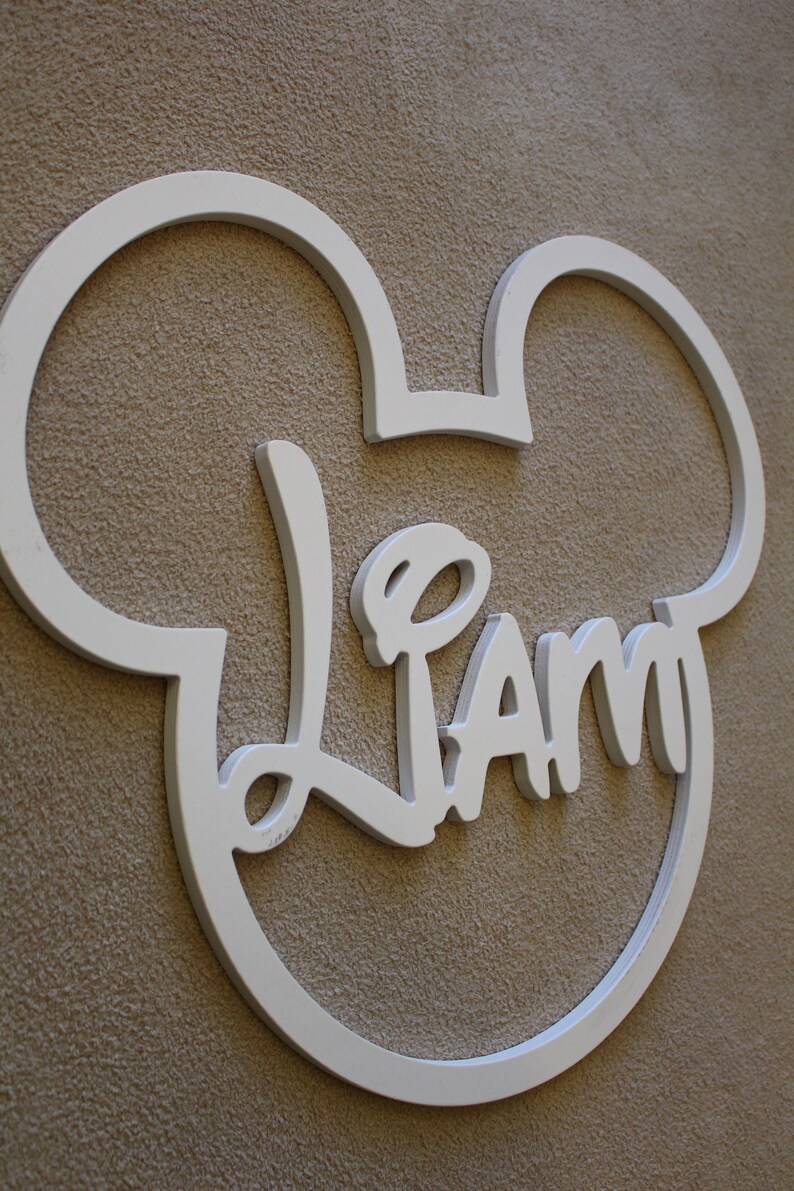 May include: White wooden Mickey Mouse-shaped sign with the name "Liam" written in a whimsical font.
