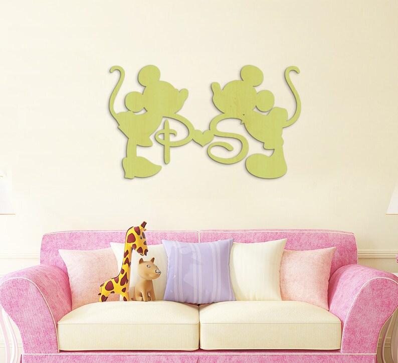 Puede incluir: Una decoraci&oacute;n de pared de madera con una silueta de Mickey Mouse y Minnie Mouse tom&aacute;ndose de la mano con las letras "P" y "S" en el medio. La decoraci&oacute;n est&aacute; pintada de color amarillo claro.