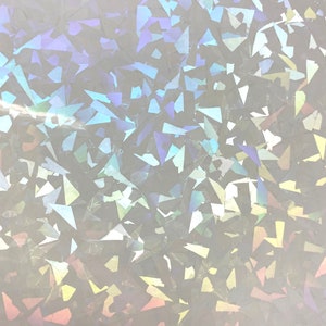 Pu&ograve; includere: Primo piano di un materiale bianco iridescente con un motivo sparso di forme geometriche irregolari. Le forme riflettono uno spettro di colori, tra cui blu, viola e giallo, creando un effetto scintillante. La consistenza generale appare liscia e riflettente.
