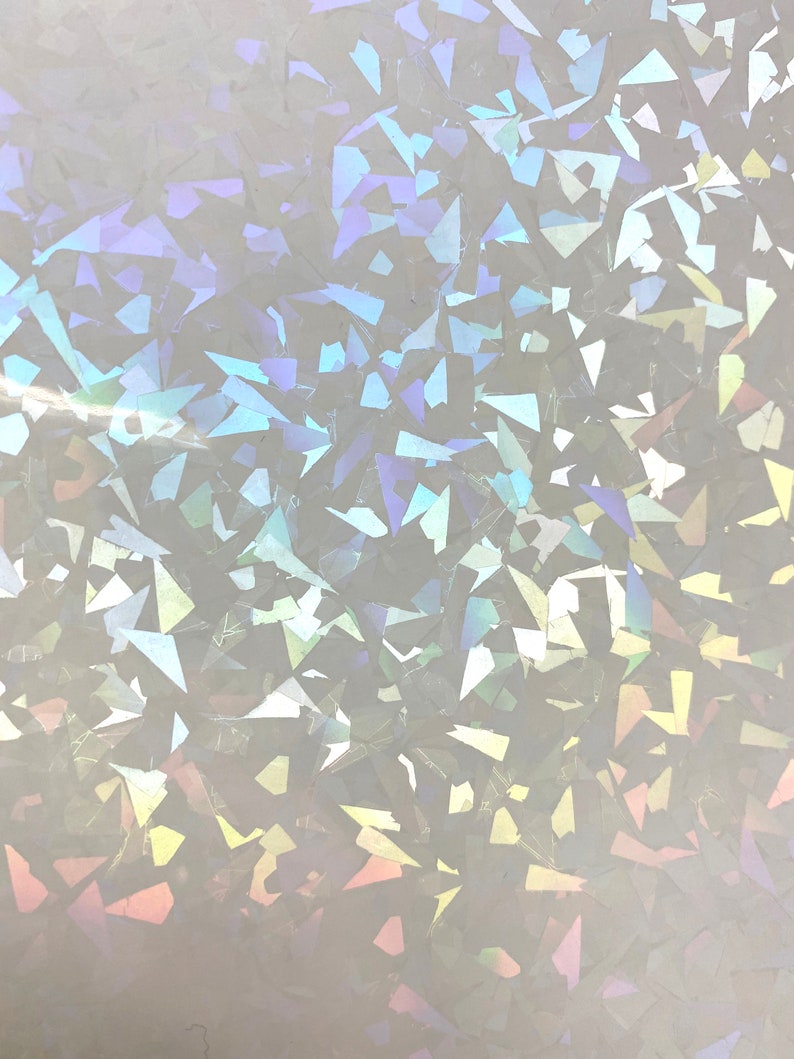 Pu&ograve; includere: Primo piano di un materiale bianco iridescente con un motivo sparso di forme geometriche irregolari. Le forme riflettono uno spettro di colori, tra cui blu, viola e giallo, creando un effetto scintillante. La consistenza generale appare liscia e riflettente.
