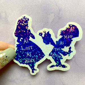 Puede incluir: Un par de pegatinas de purpurina iridiscente con siluetas de Alicia y el Sombrerero Loco de Alicia en el Pa&iacute;s de las Maravillas. El texto en las pegatinas dice "As Lost As Alice" y "As Mad As The Hatter".
