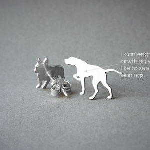 Op de afbeelding: Een paar zilveren oorbelletjes met een silhouet van een Franse Bulldog en een Duitse Korthaar. De oorbelletjes zijn afgebeeld op een grijze achtergrond. "Ik kan alles graveren wat je op de oorbelletjes wilt zien." staat op de afbeelding.