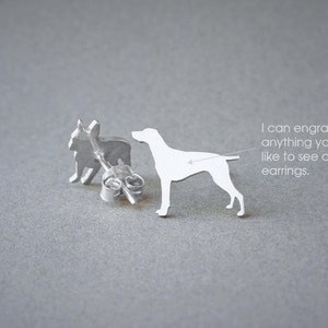 Op de afbeelding: Een paar zilveren oorbelletjes met een silhouet van een Franse Bulldog en een Duitse Korthaar. De oorbelletjes zijn afgebeeld op een grijs oppervlak. "Ik kan alles graveren wat je op de oorbelletjes wilt zien."