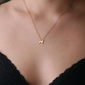 May include: A gold necklace with a dog silhouette pendant. The necklace is worn by a person with a black lace bra.
