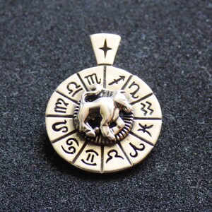 May include: Silver pendant featuring a circular zodiac wheel with a silver bull in the center. The wheel is decorated with the symbols of the twelve zodiac signs.