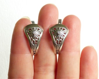 May include: A pair of silver earrings with a delicate floral design and a small clear stone in the center of each flower.