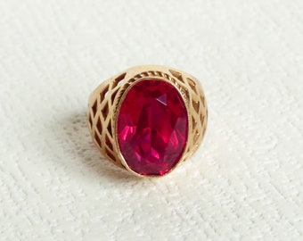 Puede incluir: Un anillo de oro con una gran piedra roja de forma ovalada engastada en un diseño decorativo de calado.