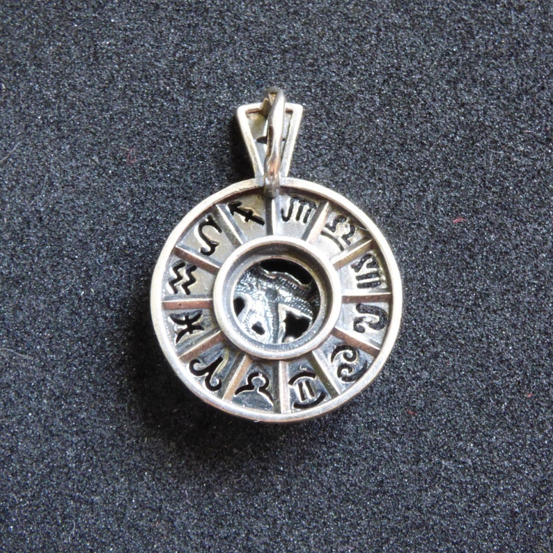 May include: Silver pendant featuring a circular design with the zodiac symbols around the edge. The center of the pendant has a cutout of a zodiac symbol.
