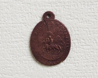 May include: A brown metal medal with a raised image of a person riding a horse. The medal has a loop at the top for hanging. The text "HONI SOIT QUI MAL Y PENSE" is inscribed around the edge.