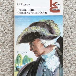 May include: A vintage book cover featuring a portrait of a man in a tricorn hat and a white ruffled shirt. The title, "Путешествие из Петербурга в Москву," is displayed in Russian text. The cover has a light beige background.
