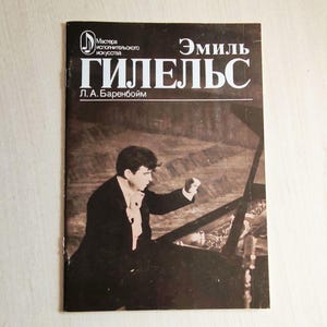 Op de afbeelding: Een vintage boekomslag met een sepia-kleurige afbeelding van een man die piano speelt. De titel "Эмиль ГИЛЕЛЬС" staat in witte letters, met extra tekst in het Russisch. De achtergrond is donkerbruin.
