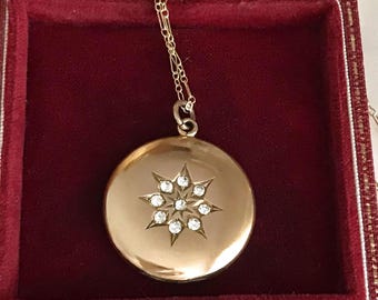 May include: A gold-colored locket necklace with a starburst design. The round pendant features a starburst pattern with clear, sparkling stones. The locket is displayed in a red velvet jewelry box, showcasing the necklace's elegance.