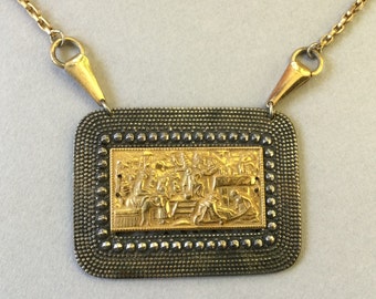 Peut inclure: Un collier avec un pendentif rectangulaire en or, avec un cadre texturé. Le cadre entoure un panneau rectangulaire plus petit avec une scène en relief détaillée de personnes dans un décor.