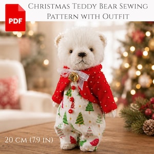 Puede incluir: Un oso de peluche blanco que lleva una chaqueta bolero roja con cuentas doradas y un mono blanco con un patrón de árboles de Navidad verdes y rojos. El oso tiene un lazo blanco con una campana dorada en el cuello y tres botones rojos al frente.
