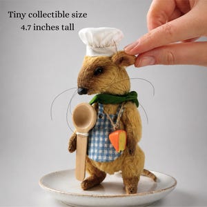 May include: A tiny, collectible plush mouse wearing a chef's hat, green scarf, and blue checkered apron. It holds a wooden spoon and a cheese pendant. The mouse is 4.7 inches tall.