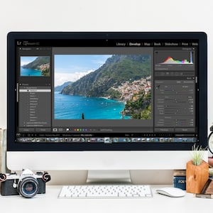 May include: A computer screen displaying the Adobe Lightroom CC software with a photo of a coastal town in Italy. The screen shows the Develop module with various editing tools and a histogram. A camera, a keyboard, and a clock are on the desk in front of the computer.