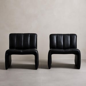 May include: Two black leather chairs with a contemporary design. Each chair features a padded back with vertical stitching and a curved, continuous frame. The chairs are set against a neutral backdrop.