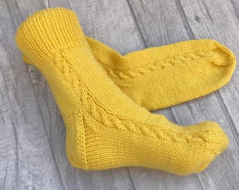 Puede incluir: Un par de calcetines de punto amarillo con un patrón de trenza.