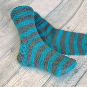 May include: A pair of blue and gray striped knitted socks. The socks are folded and lying on a wooden surface.