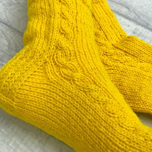 May include: A pair of yellow knitted socks with a cable knit pattern.