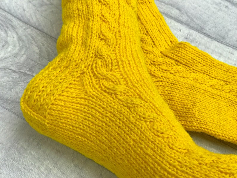 May include: A pair of yellow knitted socks with a cable knit pattern.