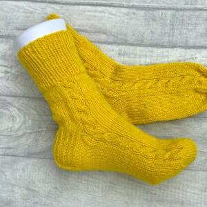 May include: A pair of yellow knitted socks with a cable knit pattern.