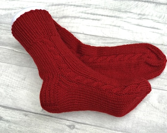 May include: A pair of red knitted socks with a cable knit pattern. The socks are folded over and the top of the socks are white.