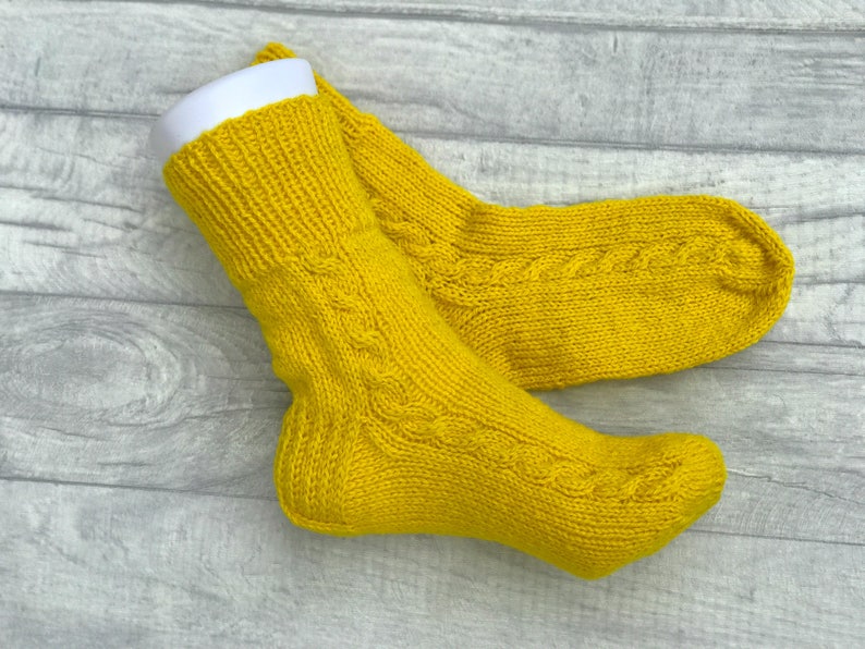 May include: A pair of yellow knitted socks with a cable knit pattern.