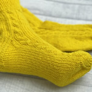 May include: A pair of yellow knitted socks with a cable knit pattern.