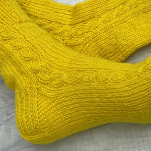 May include: A pair of yellow knitted socks with a cable knit pattern.