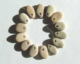 May include: A circle of 12 smooth, light brown stones with a hole drilled through each one. The stones are arranged in a circle, with the holes facing outwards.