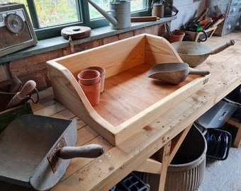 May include: A wooden tray with a scoop and three terracotta pots. The tray is sitting on a wooden workbench with a metal bucket and a black hose.