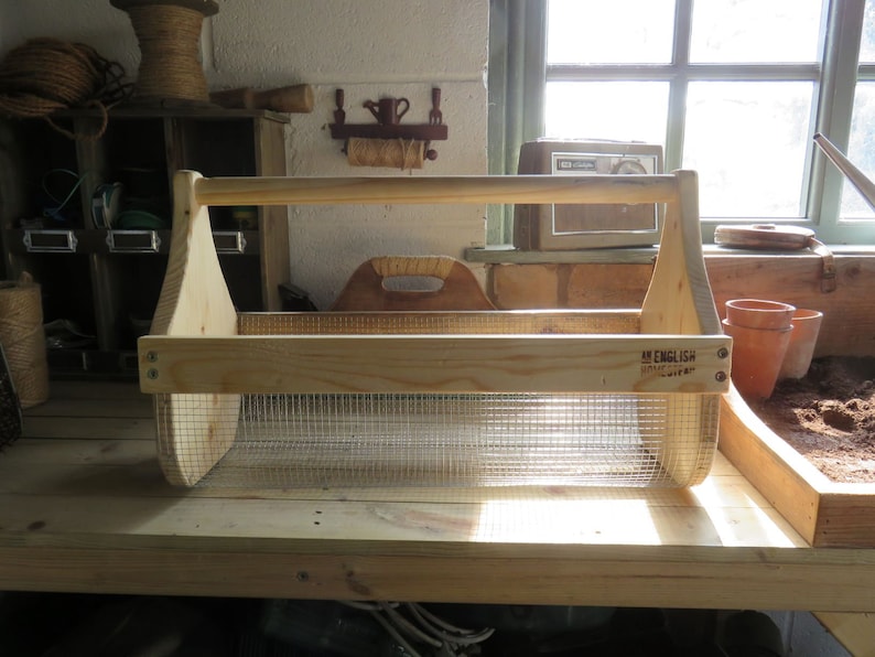 May include: A wooden gardening tool caddy with a wire mesh insert. The caddy has a handle and is labeled "An English Country Life".