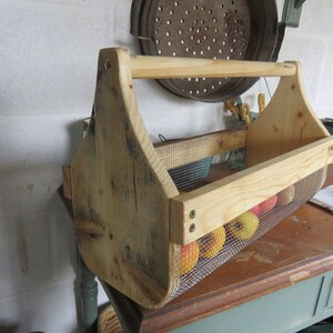 May include: A wooden carrying basket with a wire mesh insert, filled with red apples. The basket has a wooden handle and is made of reclaimed wood.