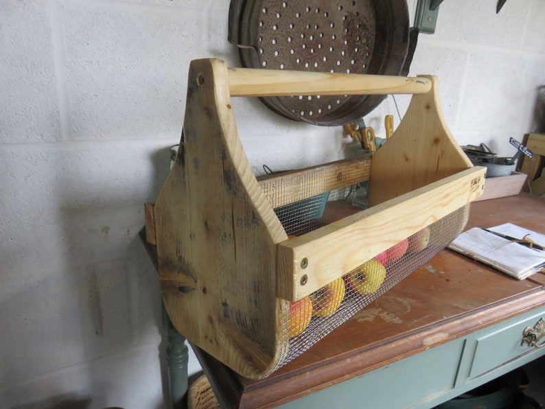 May include: A wooden carrying basket with a wire mesh insert, filled with red apples. The basket has a wooden handle and is made of reclaimed wood.