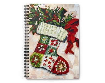 May include: A spiral-bound notebook featuring a painted Christmas stocking design. The stocking is red, green, and white, with a textured cuff and floral patterns. A sprig of holly and a red bow adorn the top, set against a neutral background.