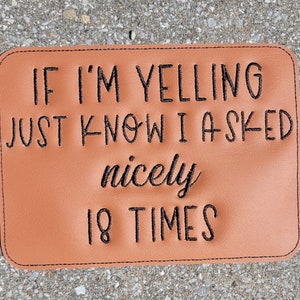 Peut inclure: Une pancarte en cuir marron avec du texte brodé en noir qui dit "Si je crie, sachez que j'ai demandé gentiment 18 fois".