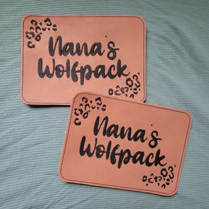 May include: Two brown leather patches with black stitching and a leopard print design. The text "Nana's Wolfpack" is embroidered in black on each patch.